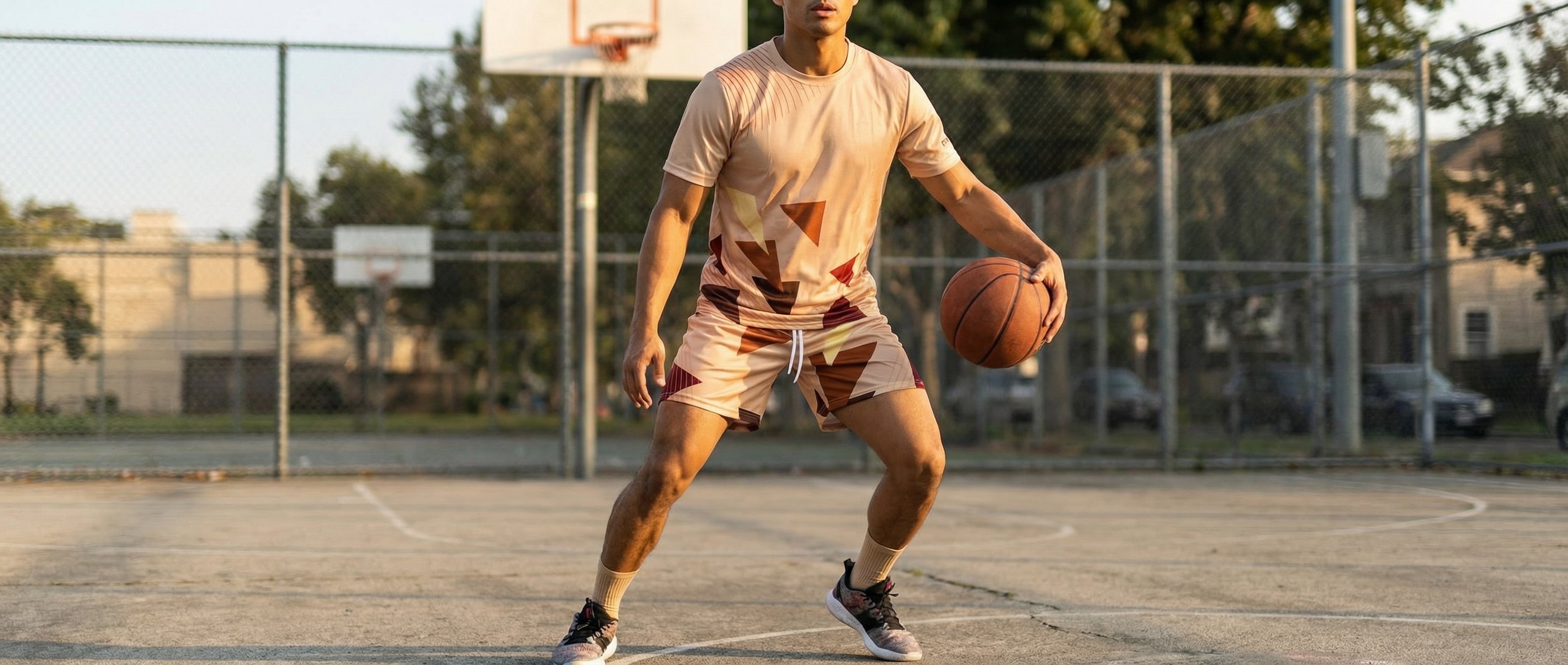 Person playing basketball on an outdoor court with a fence and trees in the background